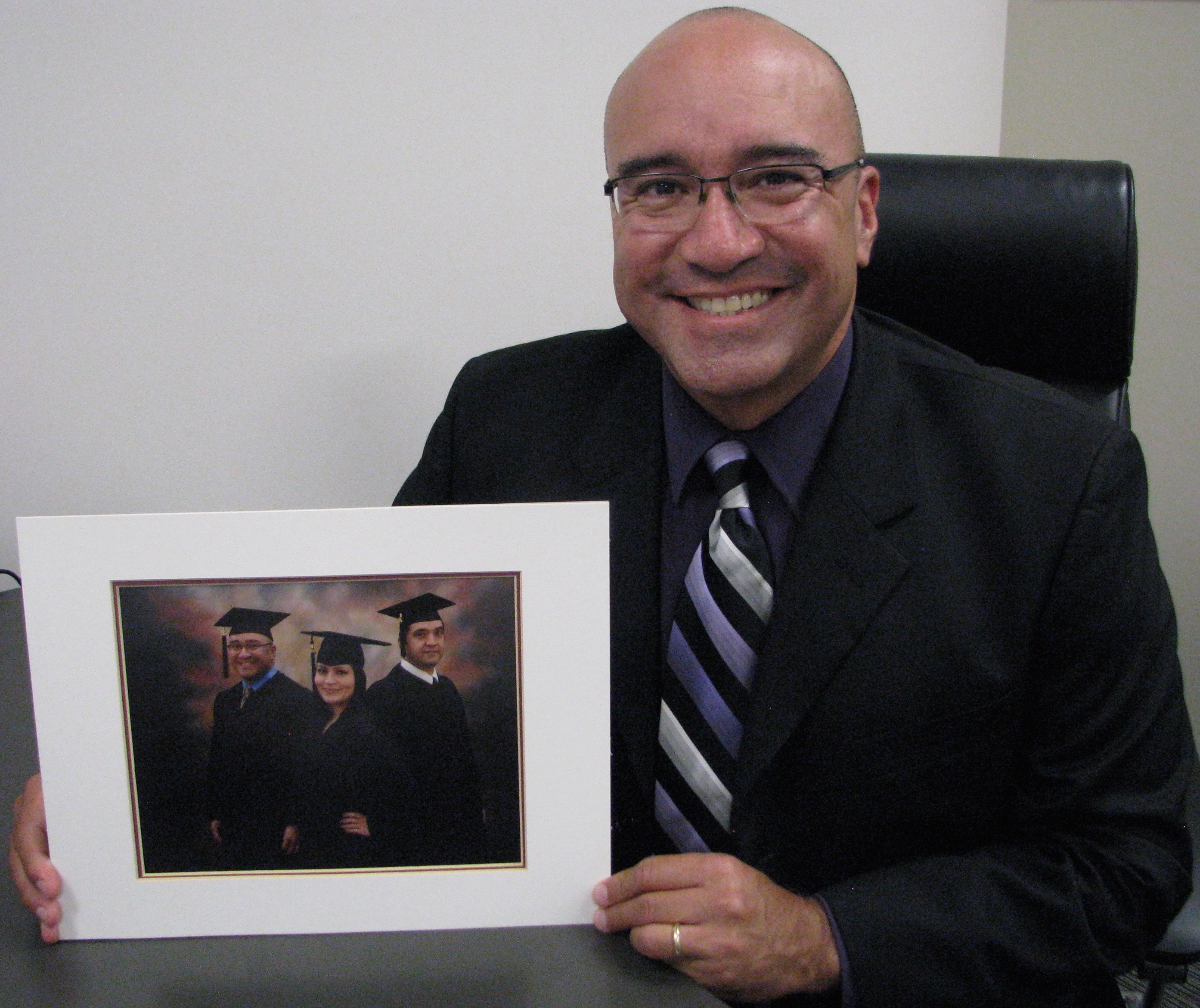 Michael Marquez (seated) holds a photo of himself, his brother Dean and his sister Cindy in graduation robes. Photo courtesy of UHCL Office of Communications.