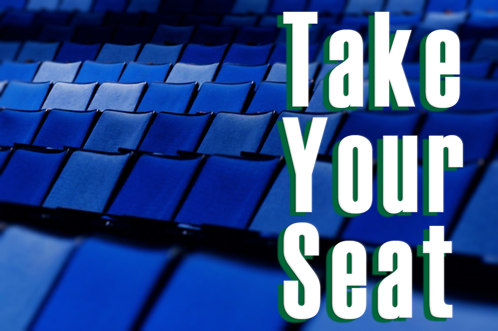 GRAPHIC: Background photo of empty blue auditorium seats with large white text in the foreground reading "Take Your Seat," with a green drop shadow. Graphic created by The Signal reporter Evan Zieschang.