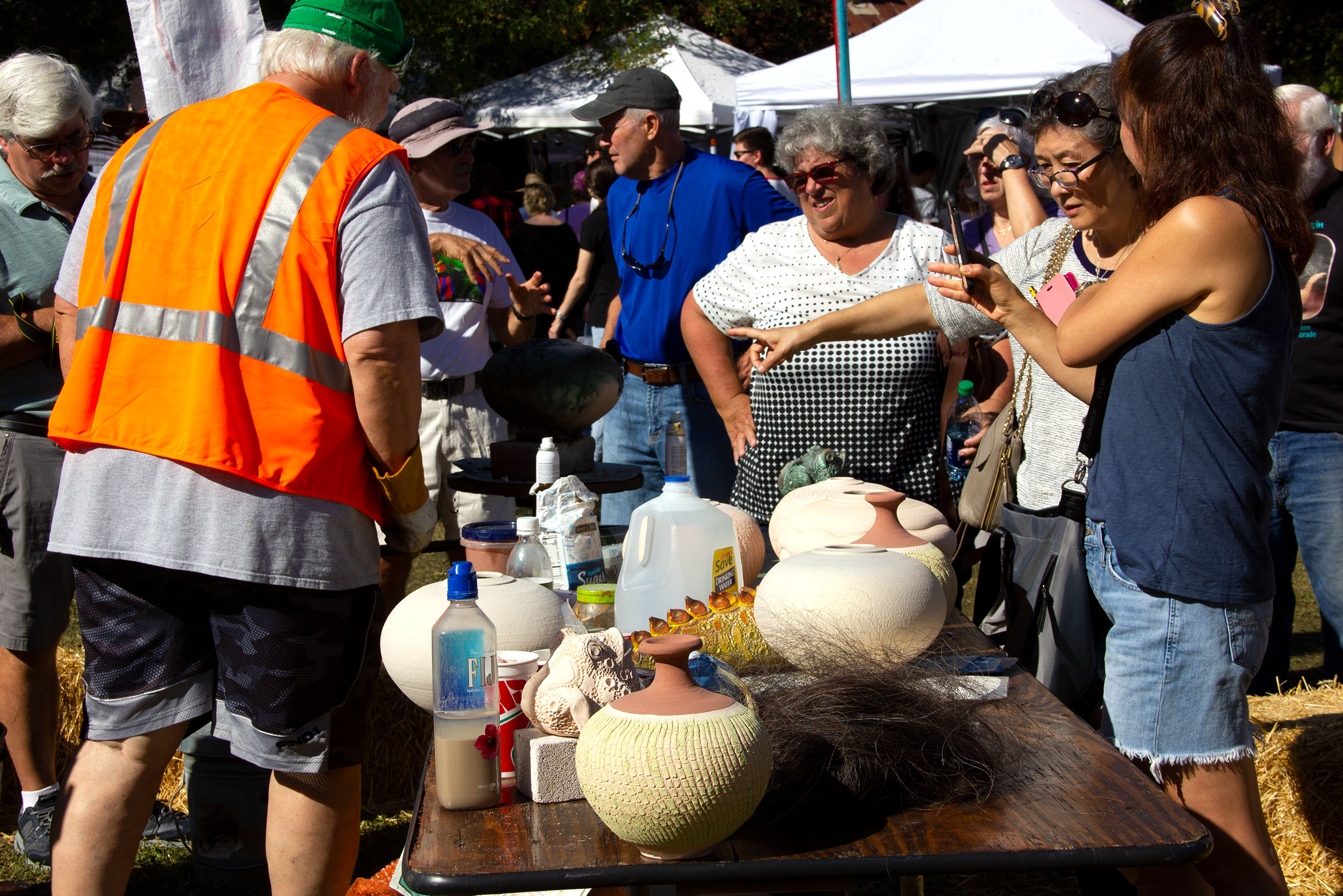 PHOTO: rodnax, in the reflective vest, gave several firing demos in the center of the festival. Across the table laid ready-to-fire ceramic piece as well as specials glazes and horse hair. Photo by The Signal Online Editor Alyssa Shotwell.