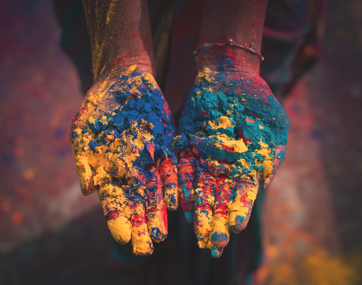 PHOTO: A woman celebrating Holy holds her colorful hands together in thanks. There are gobs of yellow, red, blue and green paint covering the palms of her hands. She is wearing a small bracelet on her left wrist. Photo courtesy of Debashis Biswas