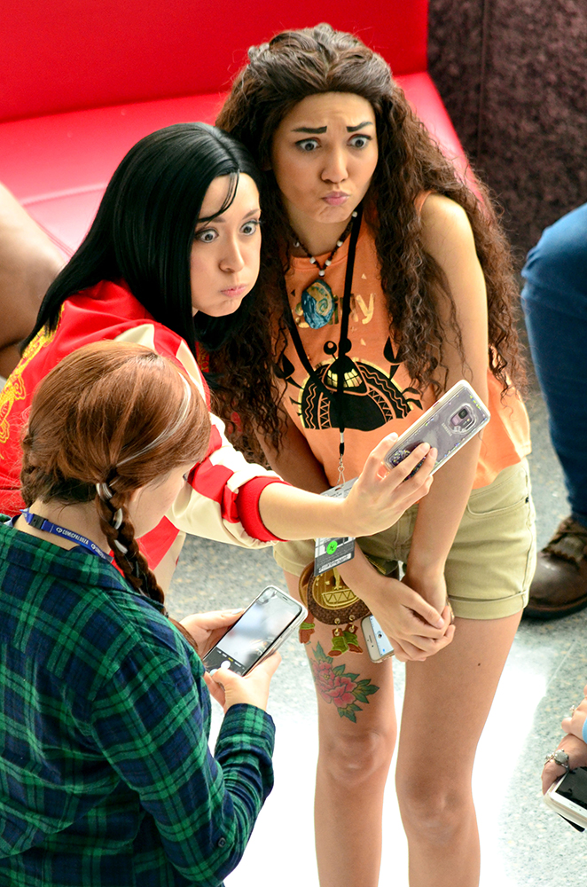 PHOTO: Two women wearing casual modern costumes designed to look like Disney’s Mulan and Moana pose for a selfie with Mulan holding a cellphone in front of them. Photo by The Signal reporter Jennifer Martinez.