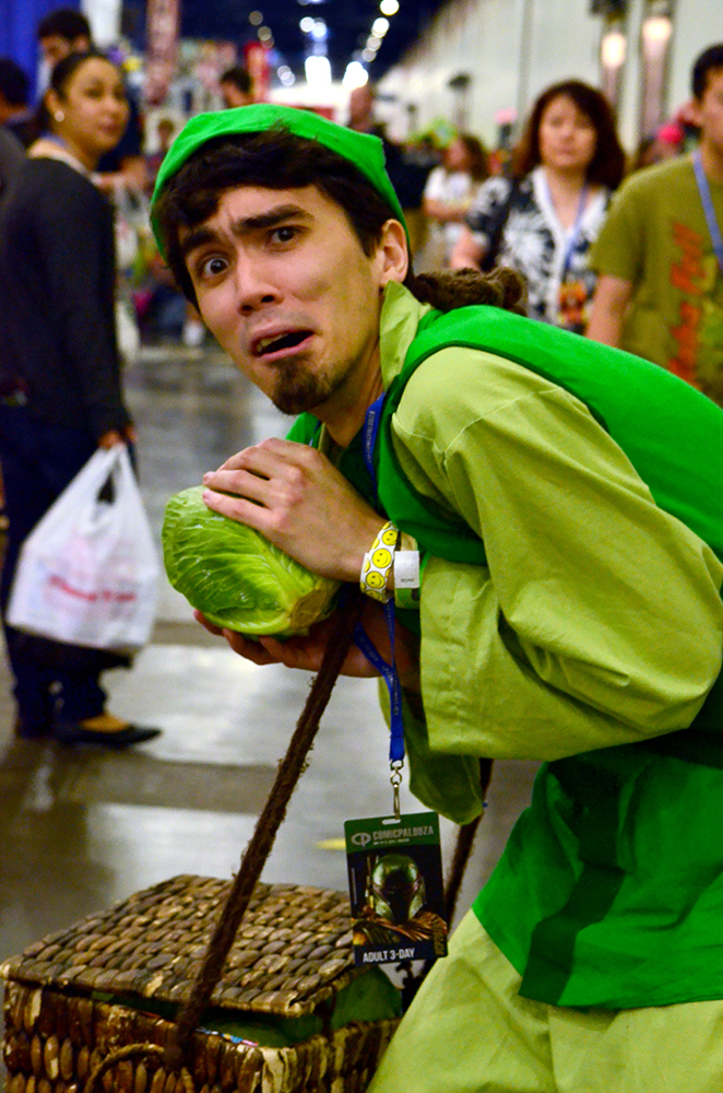 PHOTO: A man dressed in all green huddles over a fake head of cabbage while making a scared expression. Photo by The Signal reporter Jennifer Martinez.