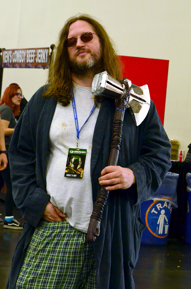 PHOTO: A man with long hair, sunglasses, a ratty robe, a dirty shirt and pajama pants poses with a toy replica of Thor’s war-ax from the Marvel Cinematic Universe. Photo by The Signal reporter Jennifer Martinez.