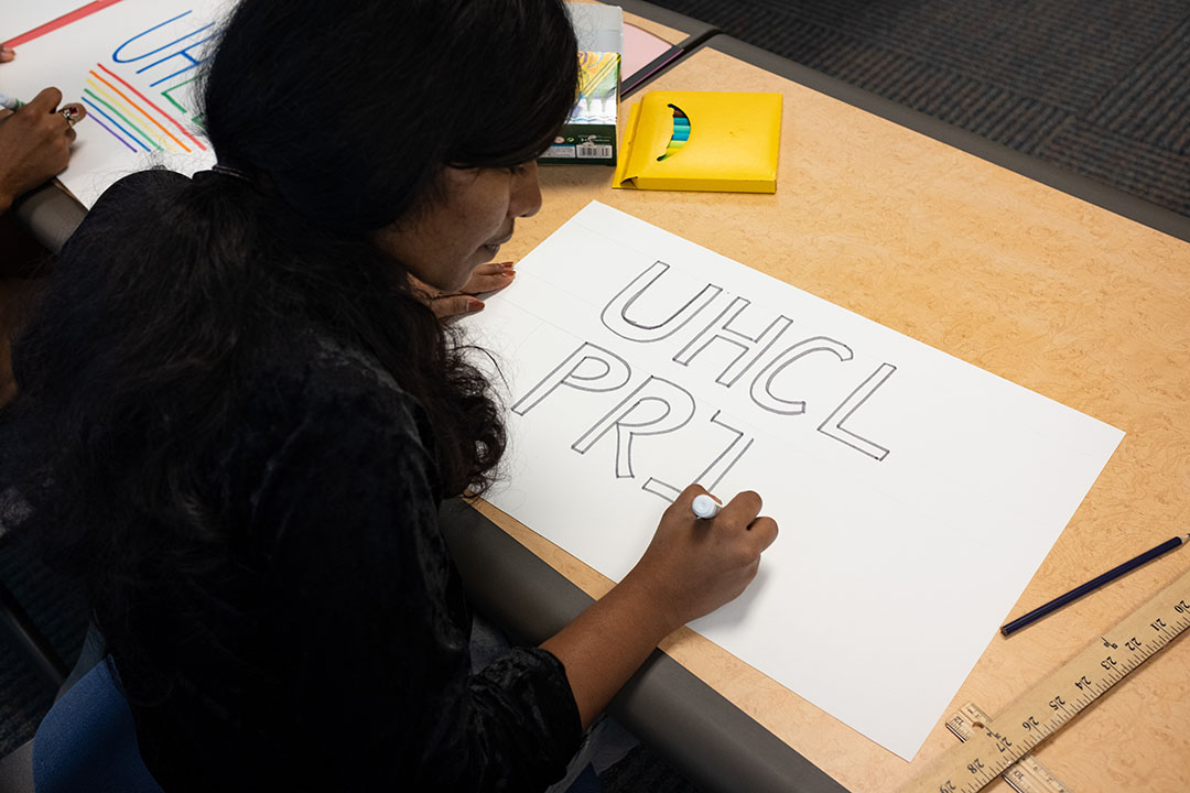 PHOTO: Student writes "UHCL Pride" on a white poster in marker. Photo by The Signal reporter Kirk McDaniel.