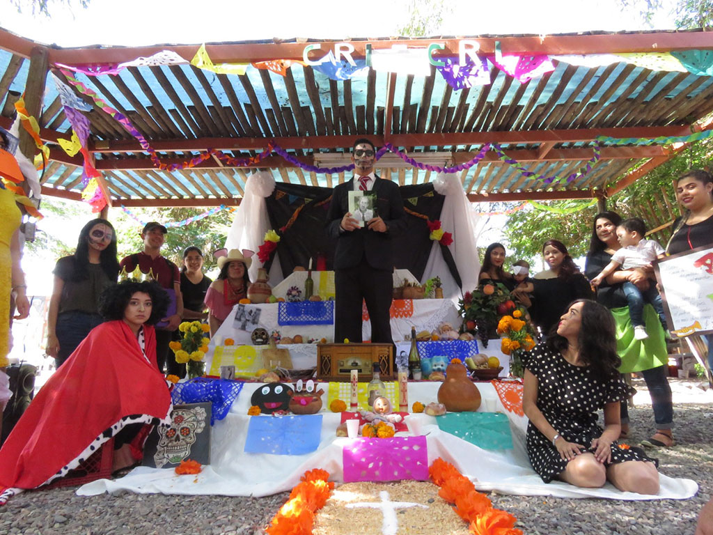 PHOTO: University of Sonora students take a group photo of a Day of the Dead altar with the family's son holding the photo of the deceased family member being honored. Photo provided by Cesar Espinoza, University of Sonora.