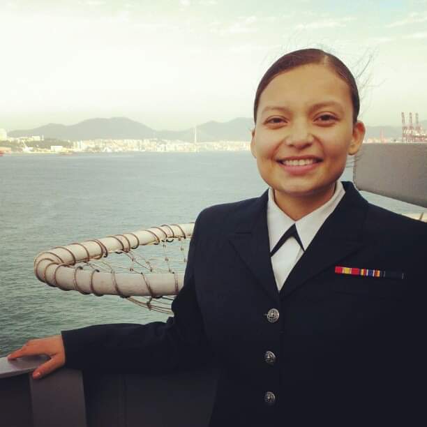 PHOTO: Photograph of veteran student Jennifer Cloud in uniform on a navy vessel while overseas. In the background, the ocean can be seen as well as mountains and a shoreline in the distance. Photo courtesy of Jennifer Cloud.