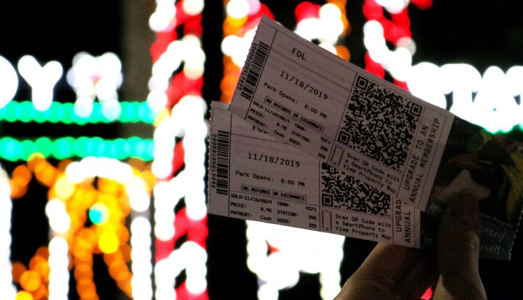 PHOTO: Two tickets to Moody Gardens Festival of Lights are shown with blurred Christmas lights in the background. Photo by The Signal reporter Emily Dundee.
