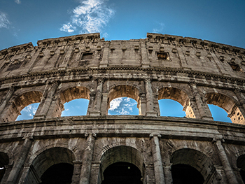 PHOTO: Photo taken from beneath the wall of the ancient Roman Colosseum, starkly contrasted against the blue sky.
