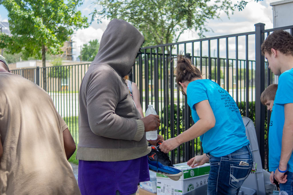 PHOTO: A woman and her son hands a homeless individual in a hooded sweatshirt shoes on a sunny day. Photo by The Signal reporter Amanda Weidle.