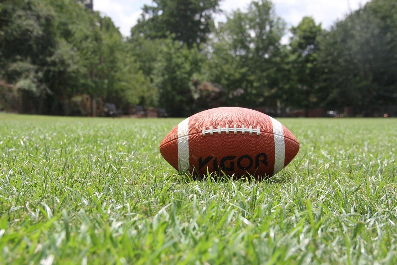 PHOTO: Football lays on grassy field. Photo courtesy of filterssofly on Pixabay. SOURCE: https://pixabay.com/photos/american-football-football-sports-1666276/