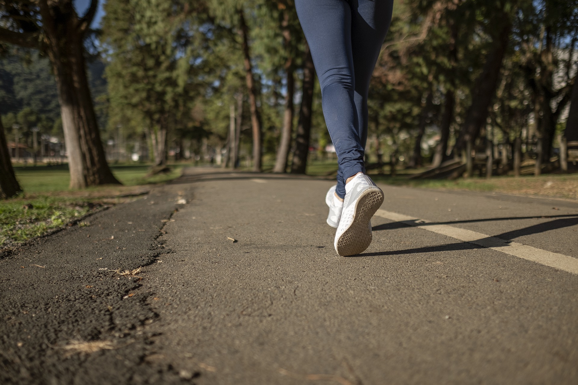 Photo: A person's legs are pictured jogging along a paved path through trees. Photo courtesy of Fotorech via Pixabay.