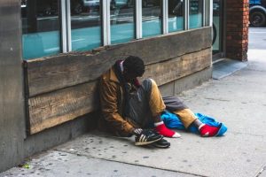 PHOTO: A homeless person sitting outside on the sidewalk. Photo courtesy of Malcolm Garret on pexelphotos.com. SOURCE: https://www.pexels.com/photo/man-sitting-on-street-2239908/