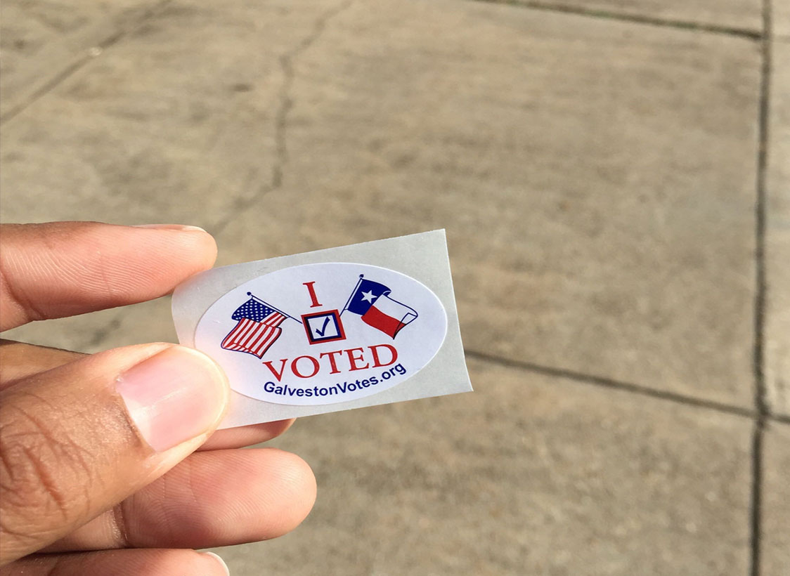 PHOTO: Image of a brown-skinned hand holding an "I Voted" sticker in the day time. Photo by The Signal Managing Editor of Content and Operations Troylon Griffin II.