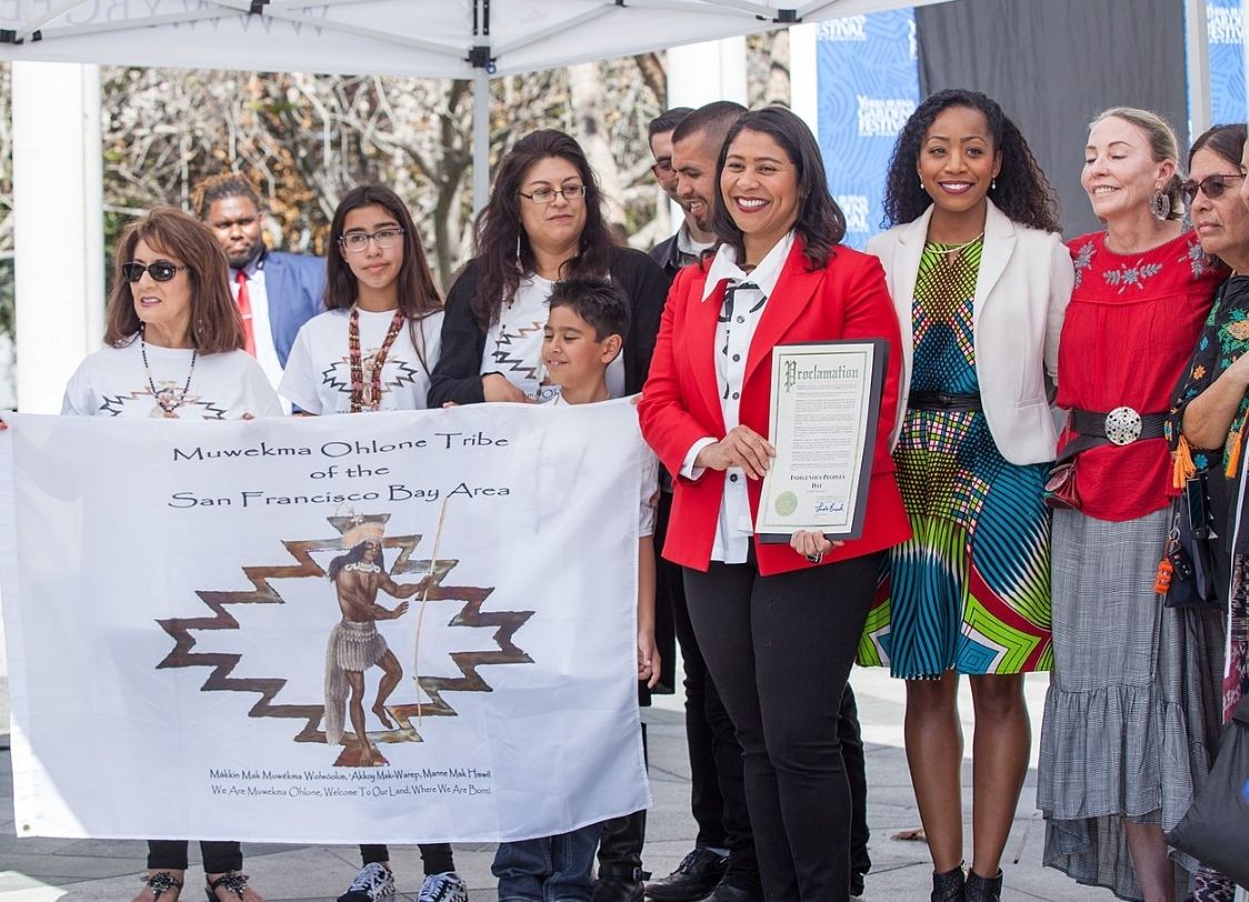 PHOTO: Members of the Muwekna Ohlone Tribe with 2018 San Francisco Mayor London Breed and two members of the Board of Supervisors at the first official Indigenous People's Day event in their city. This was taken in 2018. Photo courtesy of Pax Ahimsa Gethen. SOURCE: https://en.wikipedia.org/wiki/Ohlone#/media/File:Indigenous_Peoples'_Day_SF_20181008-5101.jpg