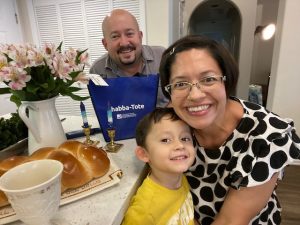 PHOTO: Image depicts man, woman and boy inside house next to bread and candles. There are also flowers and a large cup on the counter. Photo courtesy of Dr. Yvonne Hernandez-Friedman.