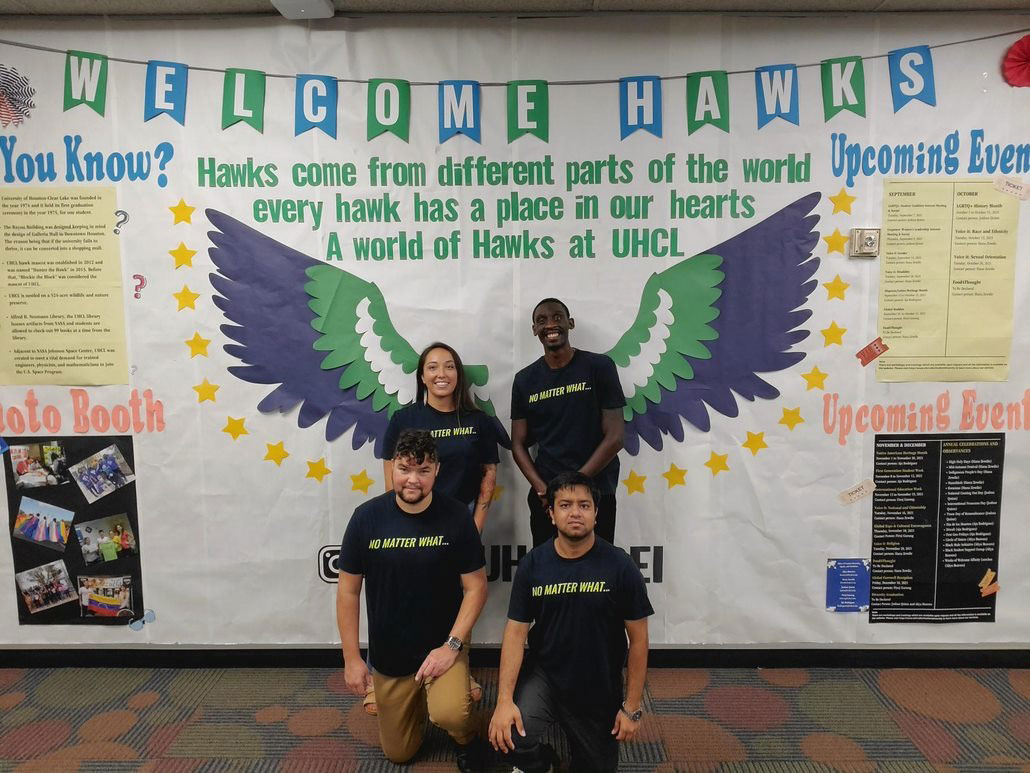 PHOTO: Image depicts SGA council in dark blue shirts that say “No Matter What.” They stand against a backdrop that says, “WELCOME HAWKS” and blue, green and white wings cut out from paper. Above them is also the words, “Hawks come from different parts of the world. Every Hawk has a place in our hearts. A world of Hawks at UHCL. Photo courtesy of SGA Vice President of Outreach & Communication Crystal Woodcock.