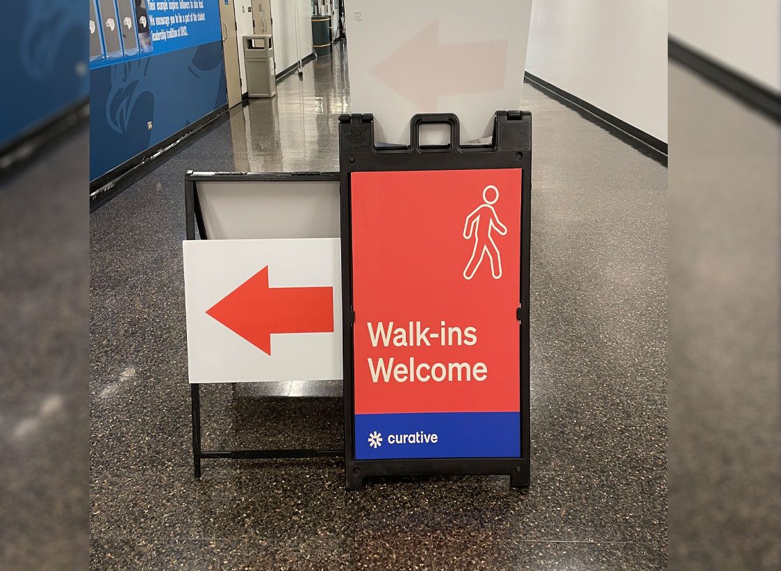 PHOTO: Image depicts a walk-in welcome sign provided by Curative in the Bayou Building for COVID-19 testings. Sign in Red and blue and has the Curative logo and the words "Walk-ins Welcome" beneath a sign of a person walking. Next to the sign is an arrow pointing to the testing room. Photo by The Signal Managing Editor of Content & Operations Troylon Griffin II.