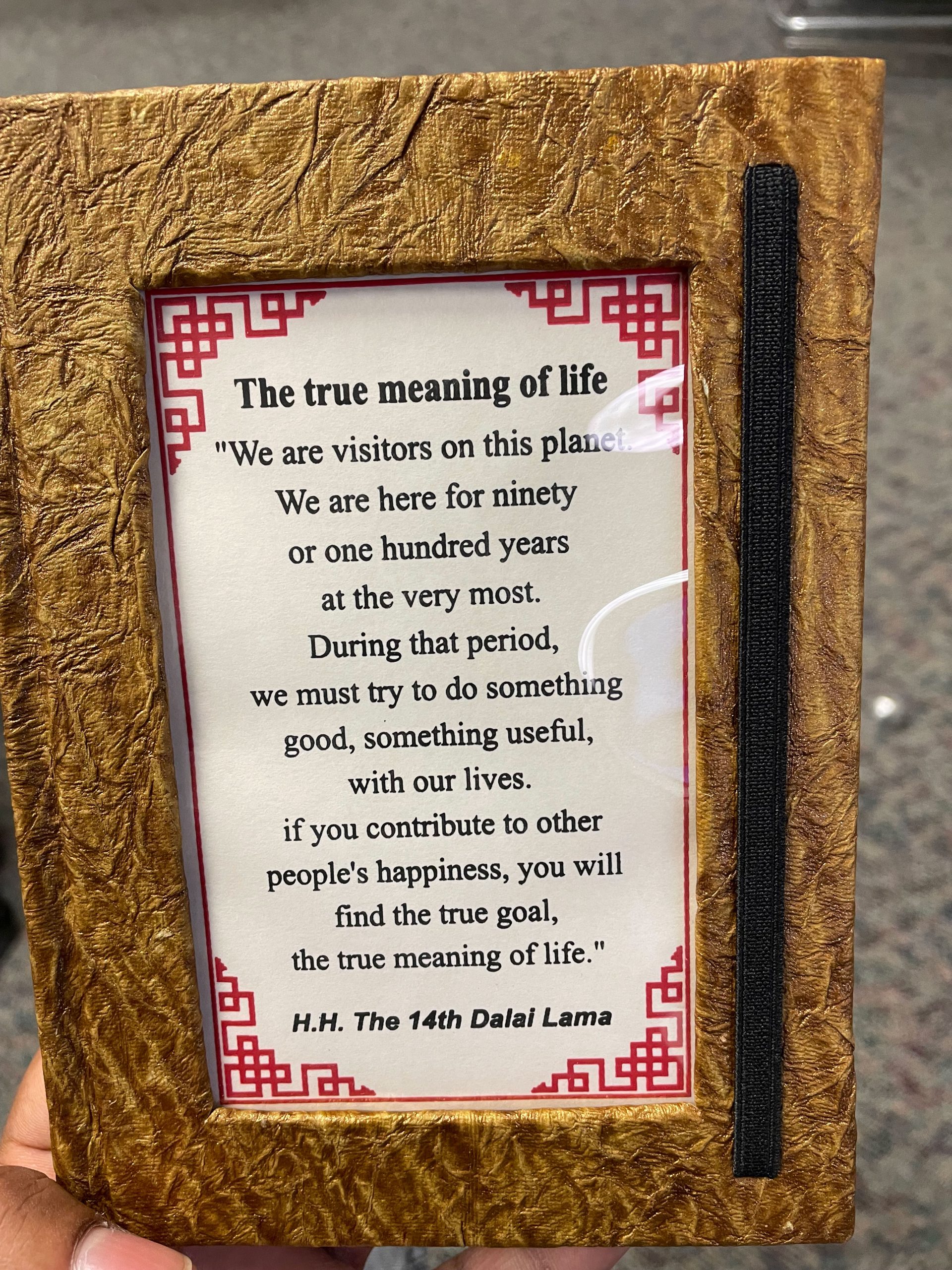 PHOTO: Image shows a brown journal being held. On the cover is a quote by the Dalai Lama on the "True Meaning of Life." Photo by The Signal Managing Editor of Content & Operations Troylon Griffin II.
