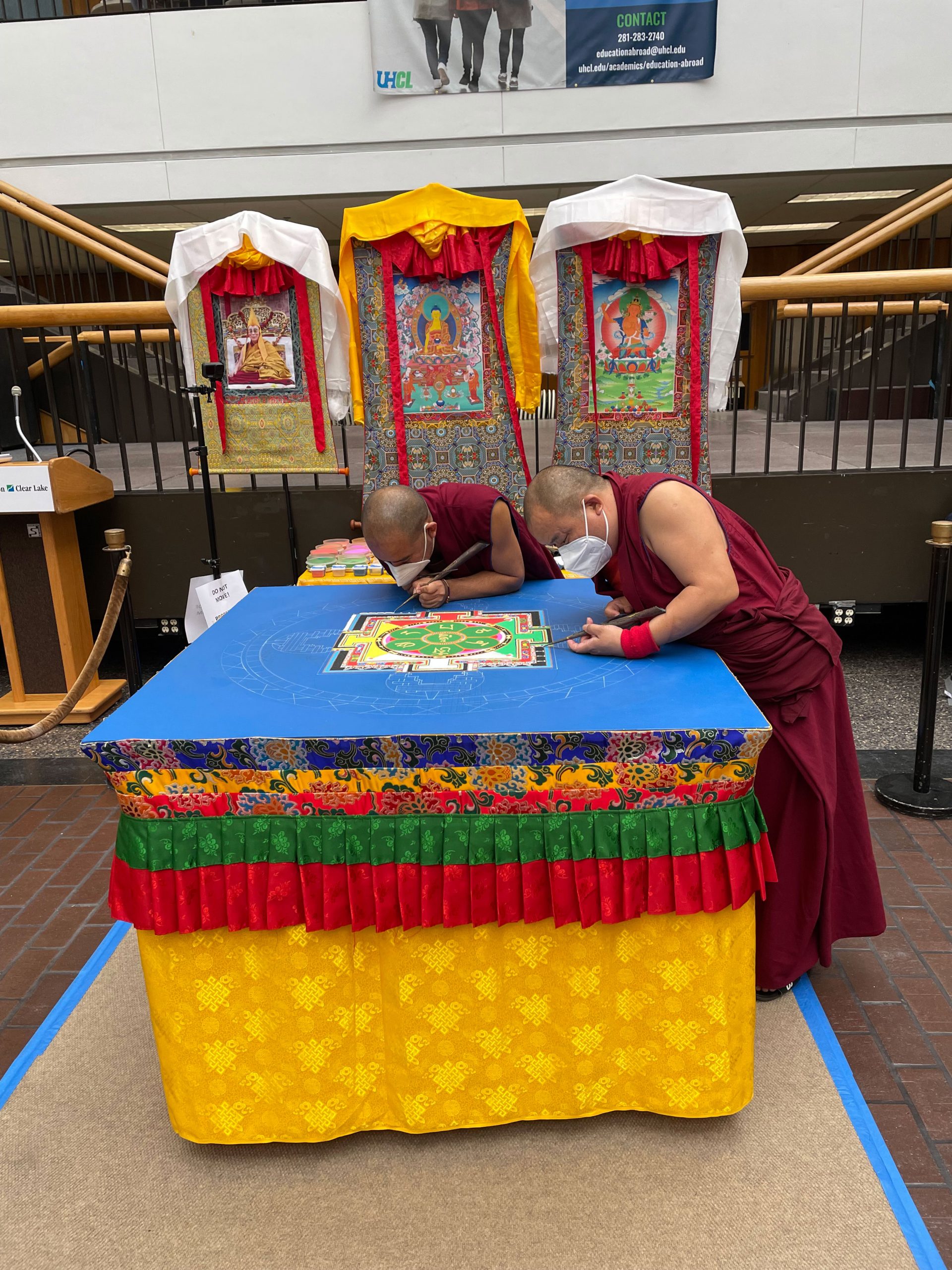 PHOTO: Image depicts Tibetan Buddhist monks working on sand mandala. Two are pictured with their tools as they stand over a table working on the design of the mandala. Photo by The Signal Managing Editor of Content & Operations Troylon Griffin II.