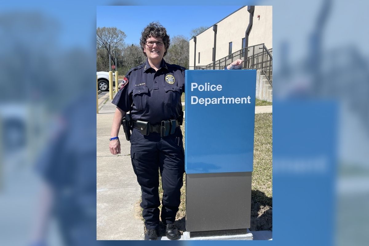 GRAPHIC: Andrea Black, Assistant Chief of Police at UHCL, standing next to campus police department signage. In the back, the image is blurred with a light blue overlay. Image courtesy of Andrea Black.