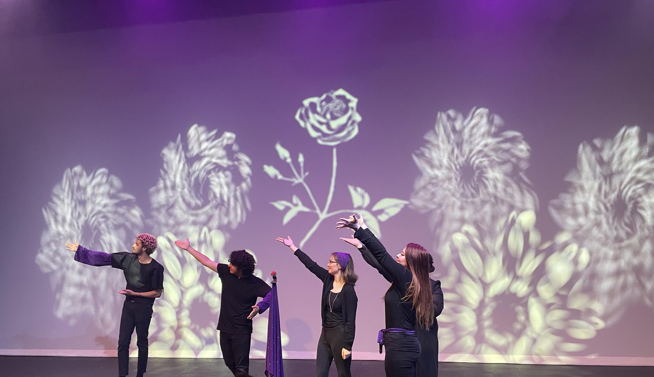 PHOTO: Image depicts casts of “The White Rose of Tejas” performers pictured from left to right: Walter McNairy, Gabriel Ismail, Mikayla Cooney, Sirena Gonzales and Ayeka Potter. The performers stand with their hands up in front of a purple backdrop, with white roses on the walls. Photo by The Signal Managing Editor of Content & Operations.
