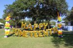 Happy Juneteenth is spelt out, with happy on top, with gold balloons. The gold balloons are flanked by a column of you balloons colored white, green, orange, and purple. The set up is on the grass with a tree behind it. A popular location for photos during the event. Photograph by The Signal reporter Jared Cadore.