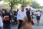 O'Rourke is wearing a white button up shirt and black pants. He is smiling down as he speaks with a woman sporting braids and a brown shirt. Behind them we see people going about their business talking and walking around the park. Photograph by The Signal reporter Jared Cadore.