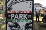 The sign is in a portrait style. The main background is white with black drawings in the style of a face. The word Emancipation is in red, park beneath it is in white, conservancy is beneath in green. Park is on a black background with "Est." on its and 1872 on its right. Photograph by The Signal reporter Jared Cadore.