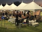 Its night time in this photo. People are lined up at multiple tents selling food such as fish, bbq, and shaved ice. This is taken from behind five of the tent where staff can be seen working as well as people in front ordering food. Photograph by The Signal reporter Jared Cadore.