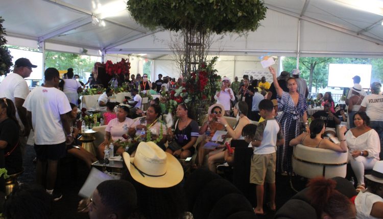 The VIP section is under a single large white tent. This is where local politicians, community leaders, celebrities, and others came for fellowship. There are numerous people standing, sitting, and talking. A tree is near the center of the tent and is visible in the photo. In the back and left tables can be seen where drinks and food are served. Photograph by The Signal reporter Jared Cadore.