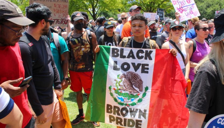 PHOTO: A protester surrounded by a crowd of fellow protesters holds up a Mexican flag with the words “Black Love Brown Pride” written on the flag. Photograph by The Signal Managing Editor Cesar Cardenas.