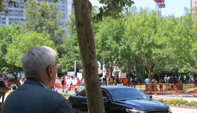 PHOTO: A man stands in front of a group of protesters from a distance. A black police car sits on the road between the man and the protesters .Photograph by The Signal Managing Editor Cesar Cardenas.
