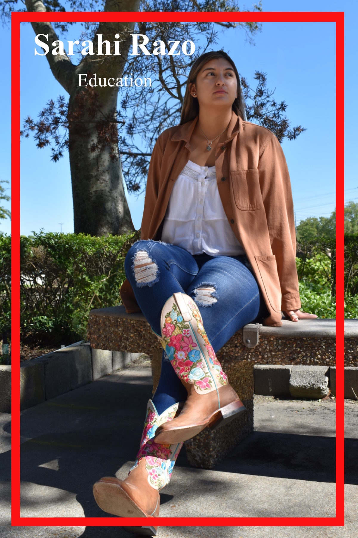 Sarahi Razo, Education Major, sitting cross-legged on a concrete bench outside of the Patio Café. Wearing a white lace blouse and ripped jeans, she finishes the look with a tan khaki jacked, and matching cowgirl boots with vibrant primary colored embroidered flowers.