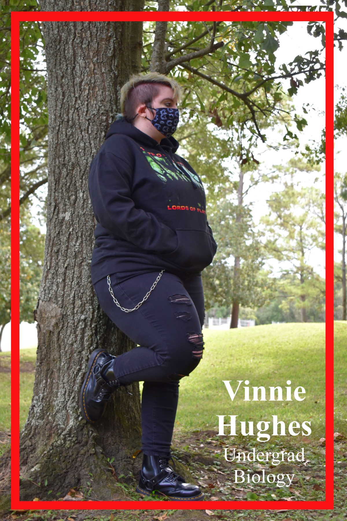 Vinnie Hughes, Undergrad in Biology, resting against a tree outside of Bayou Building. Dressed in all black attire with a graphic hoodie, ripped jeans and chain, boots, and a graphic mask to complete the ensemble.