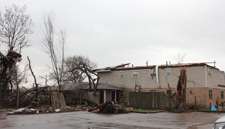 A building in Deer Park with the roof missing, a tree snapped in half, and debris in the trees.