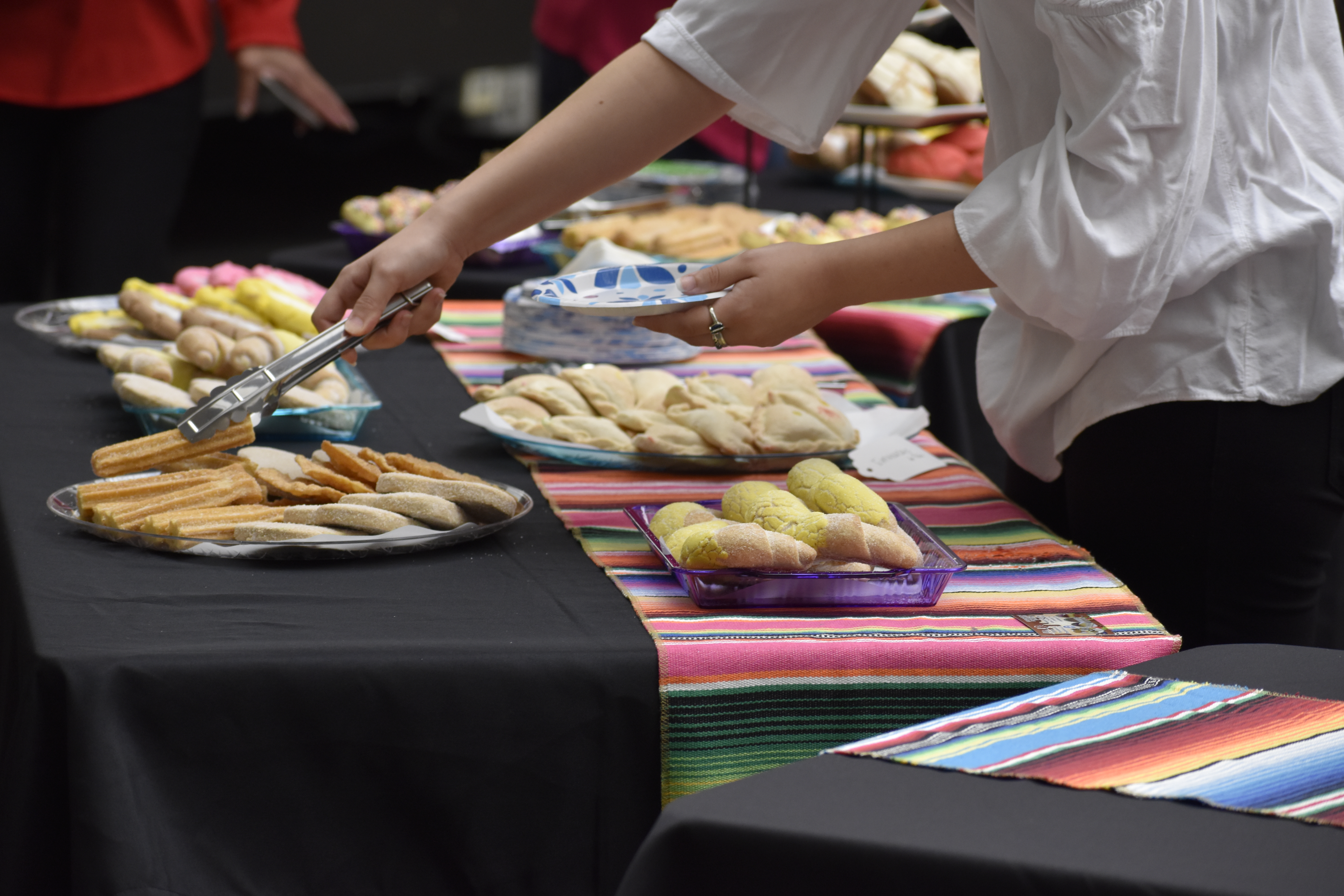 A person using tongs to get a churro from a table of many Hispanic desserts and treats.