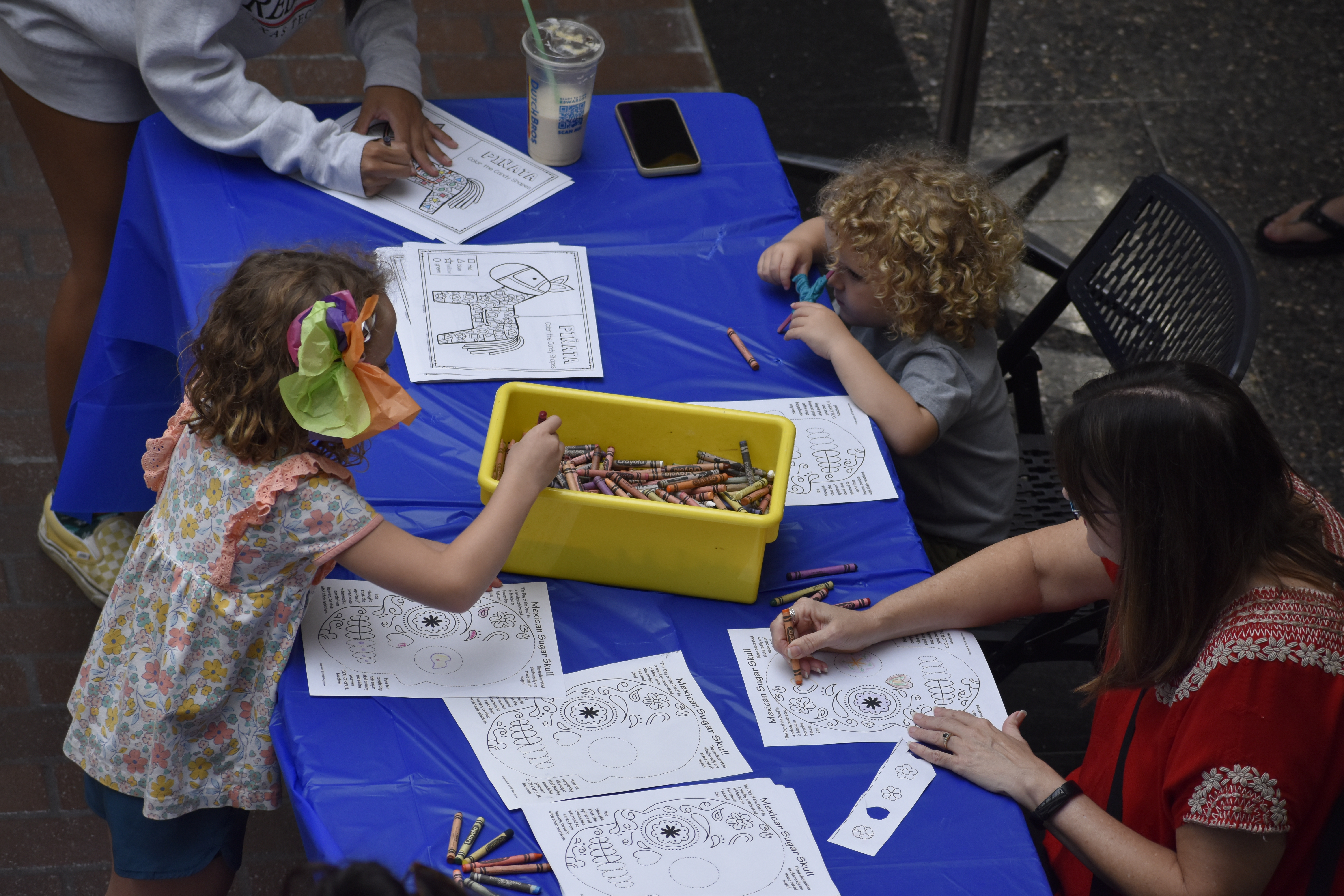 Two adults and children drawing and coloring sugar skulls.