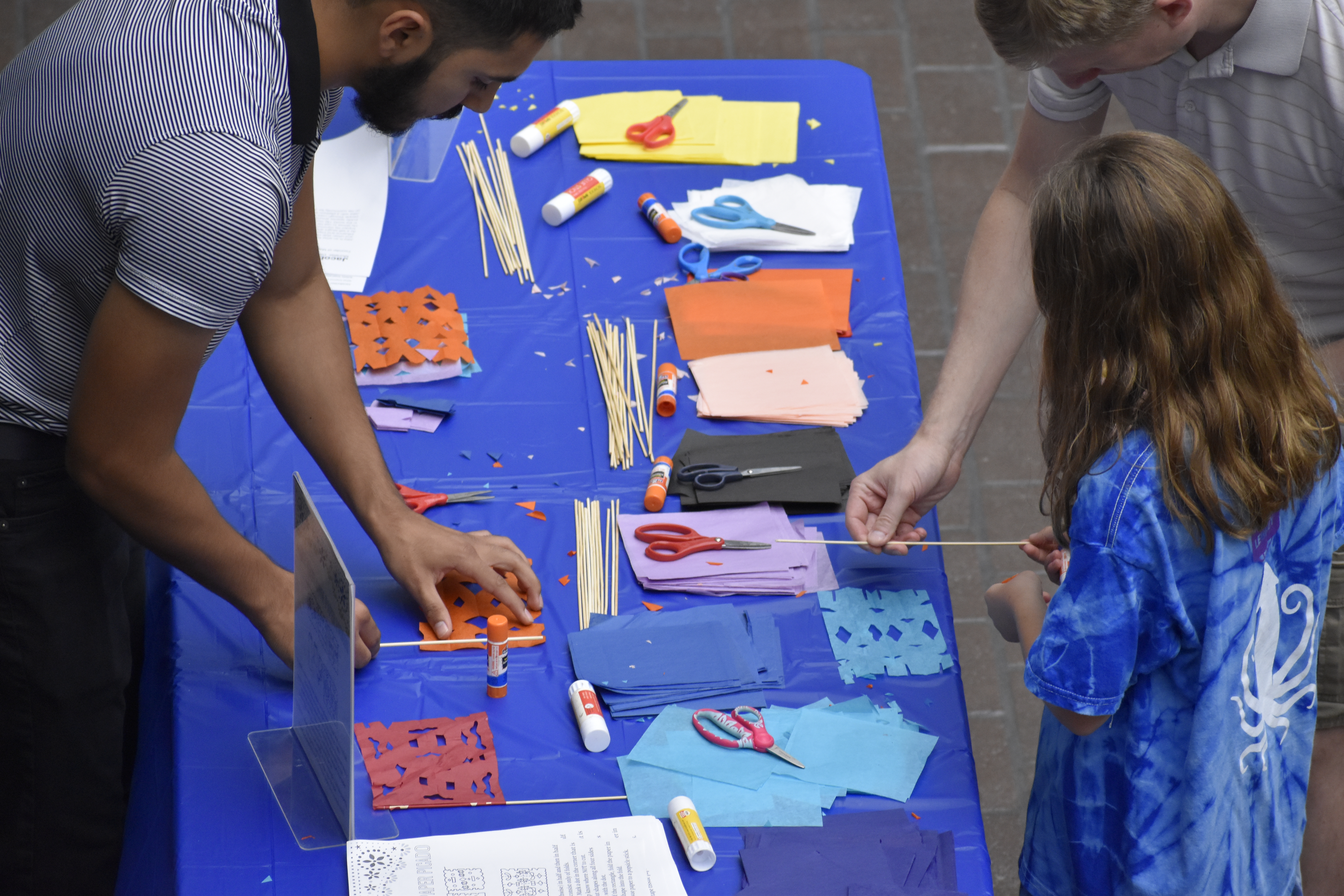 A father and child being taught how to make Papel picado (chopped paper banners).
